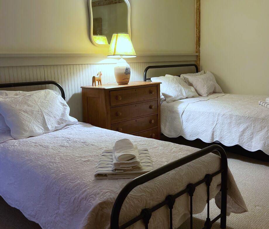 Bedroom with iron bed frames, white quilts and a wooden dresser