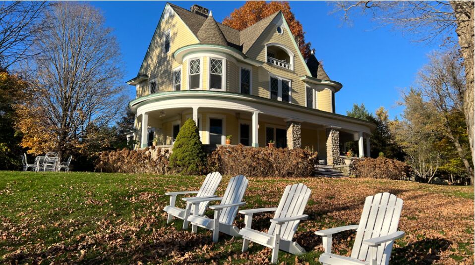 The main house in autumn with white Adirondack chairs on the lawn