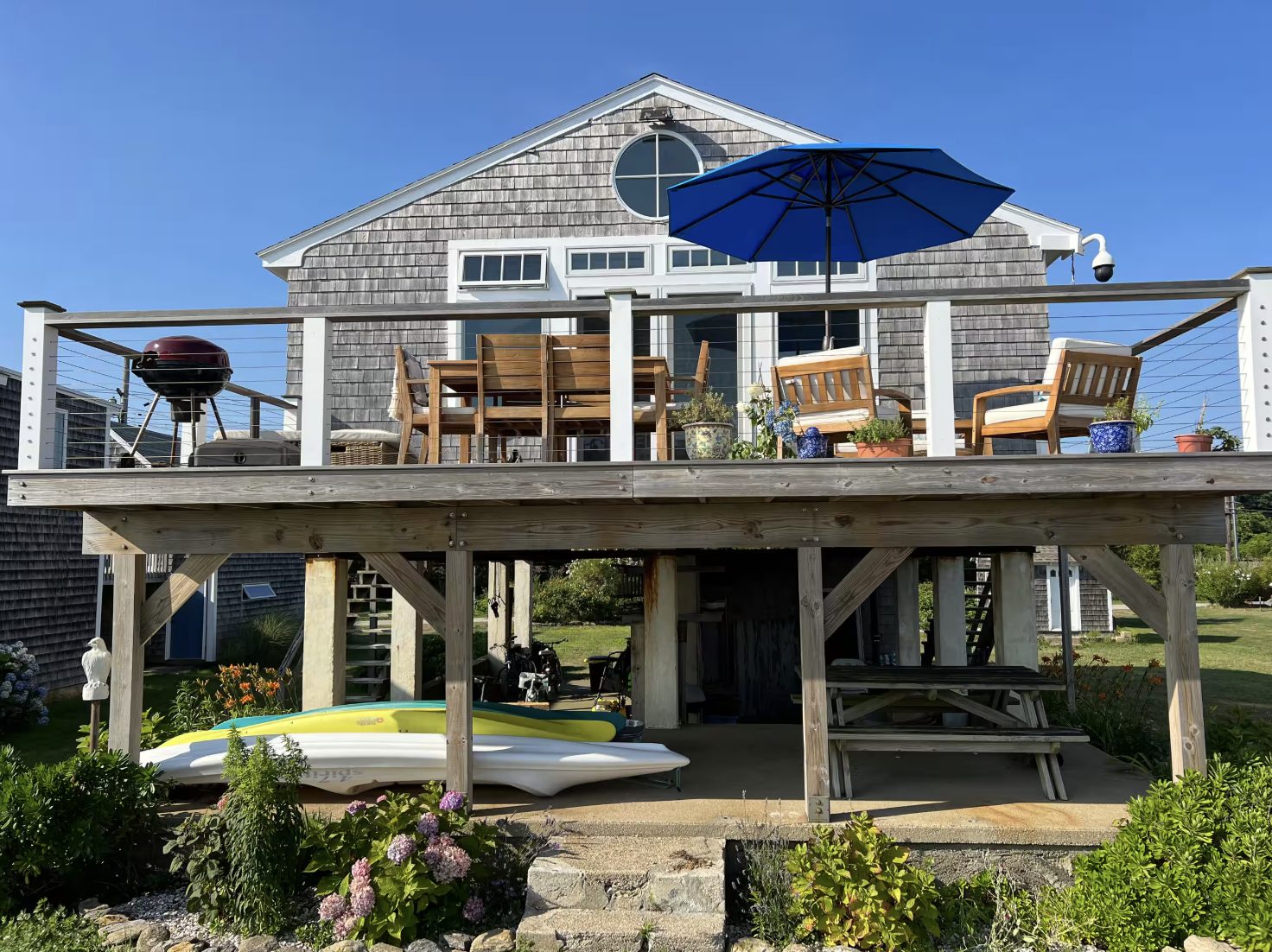 Shingled cottage on stilts with its deck above and kayaks below