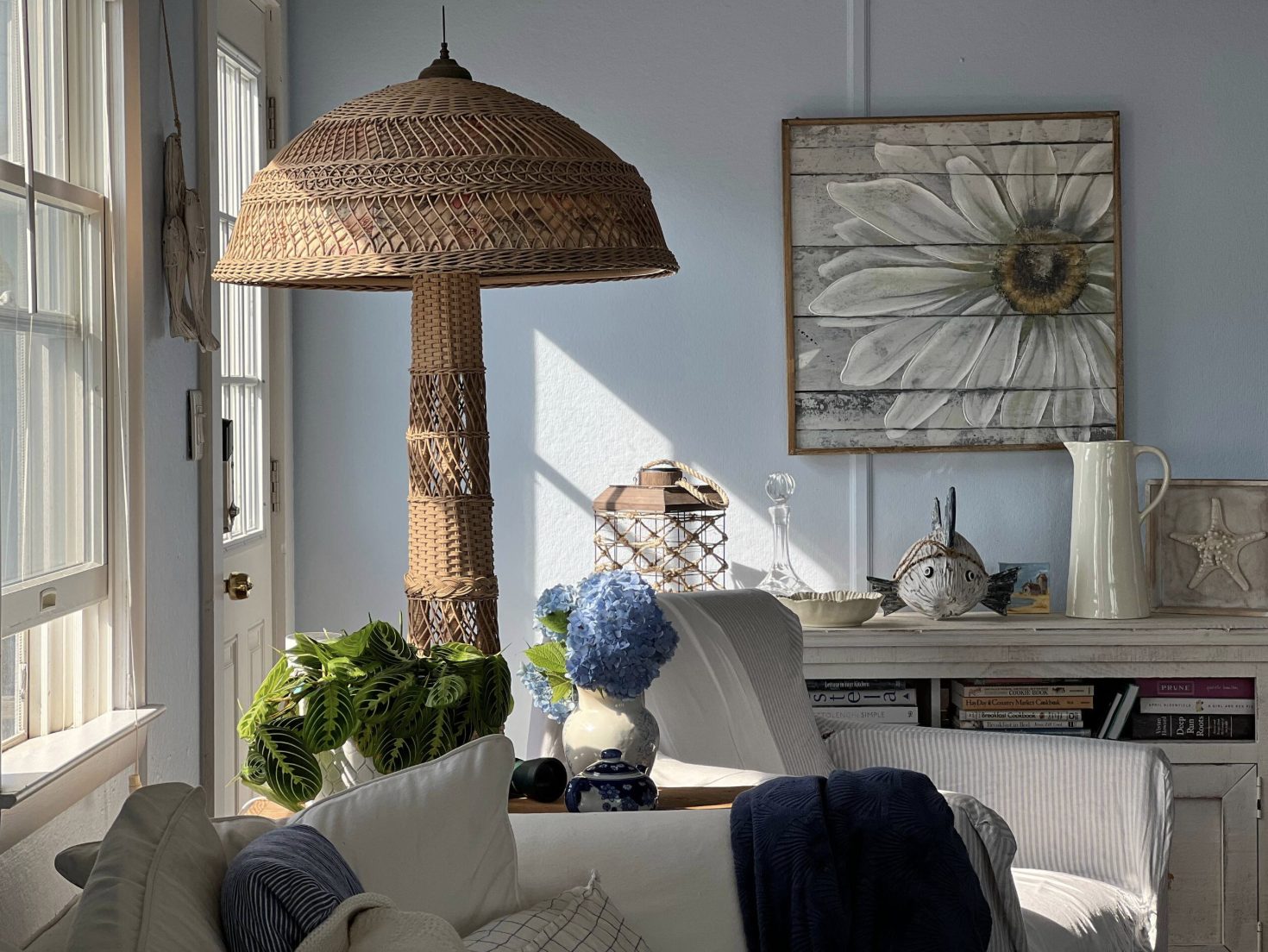 Sunlit living room with a large wicker lamp, blue hydrangeas and a white slipcovered sofa