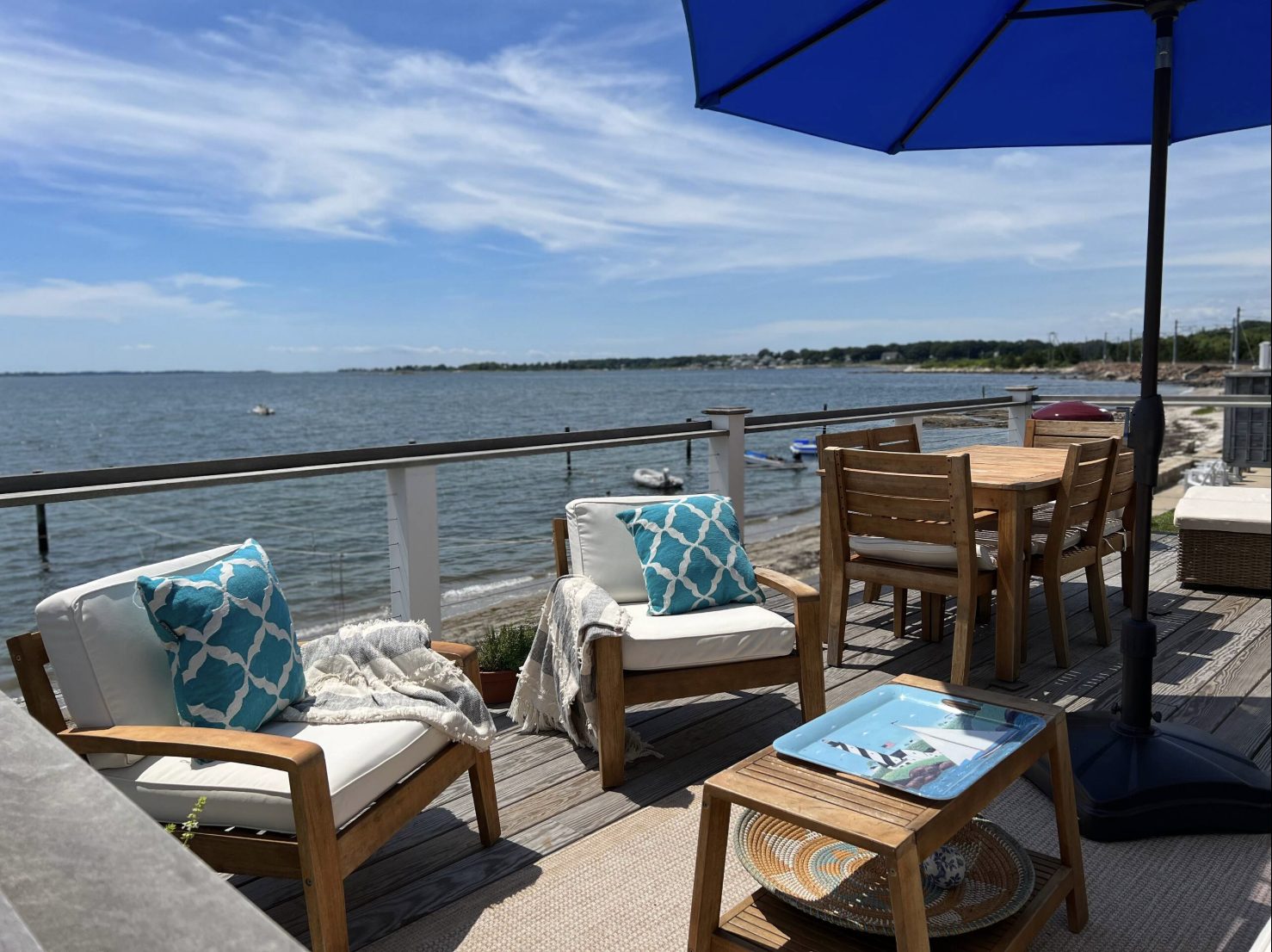 Oceanfront deck with teak chairs and a blue umbrella overlooking the water