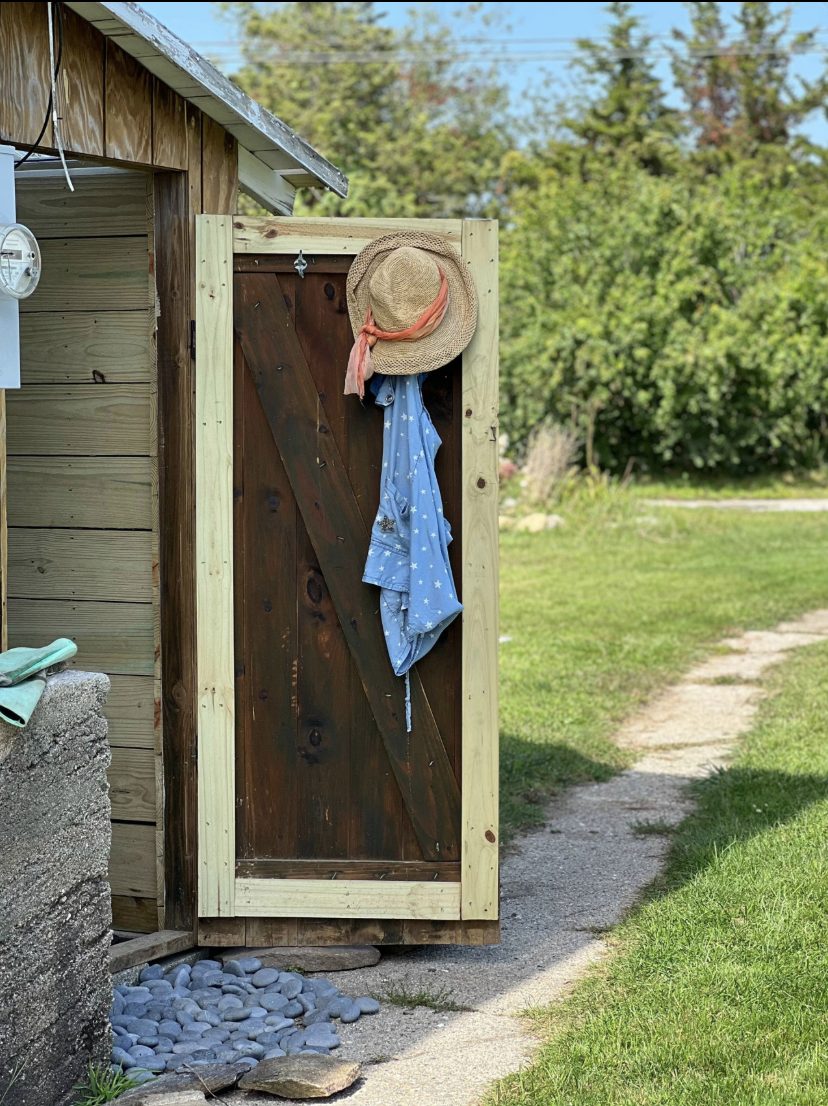 Wooden outdoor shower with a sun hat hanging on the door